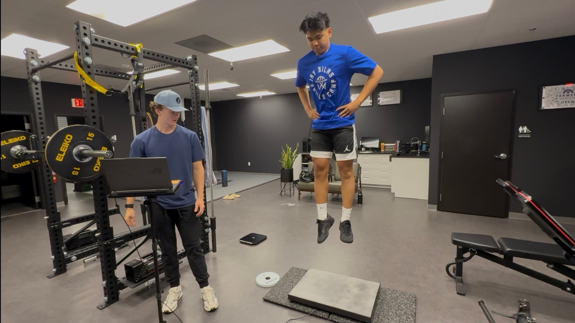 Athlete performing a force plate jump while coach monitors data